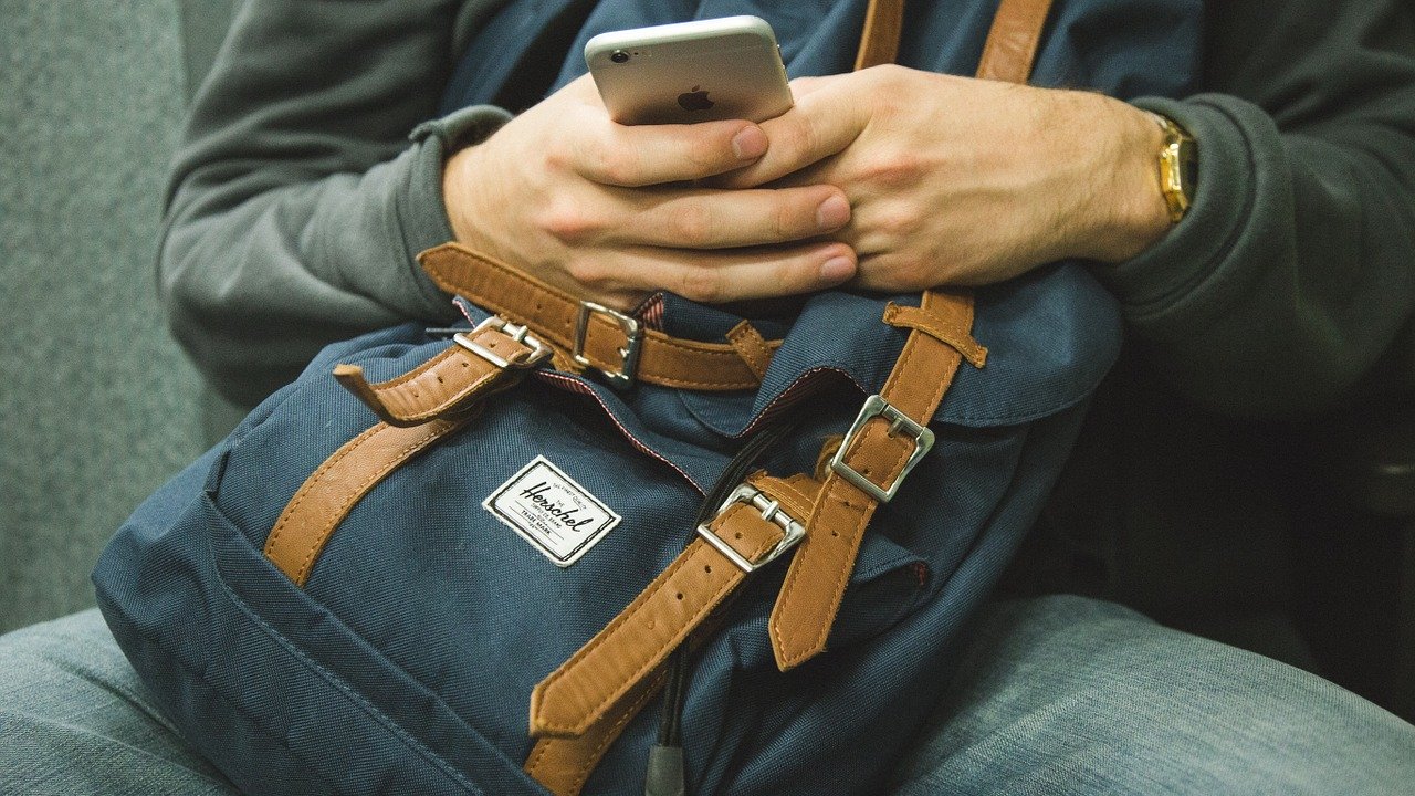 person holding a back pack while scrolling through phone